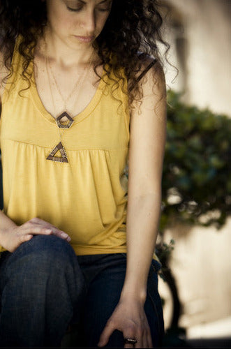 Woman wearing a yellow sleeveless top with a necklace, sitting outdoors.