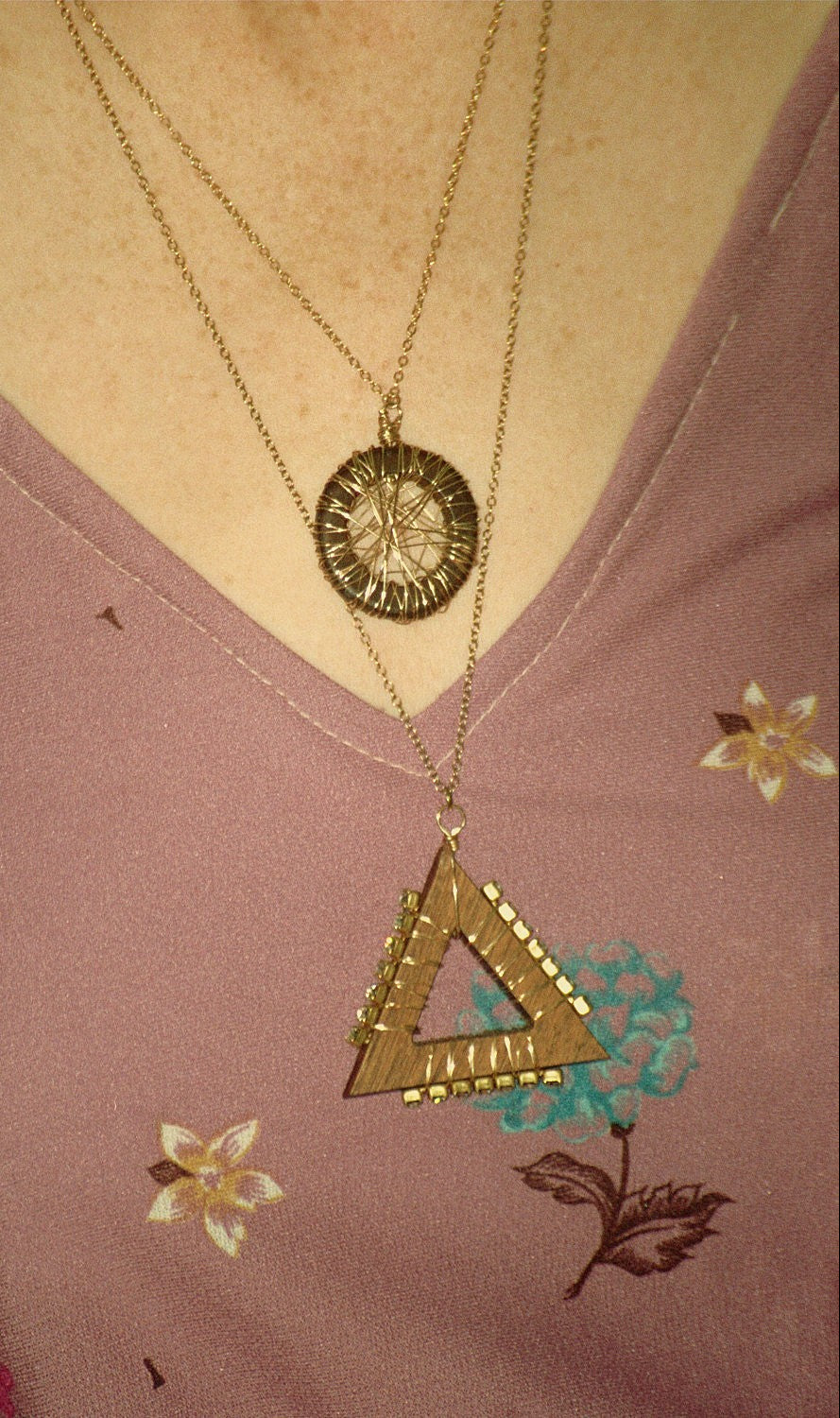 Handcarved walnut wood triangular necklace with gold plated wire and cz. Shown on a pink top with floral patterns